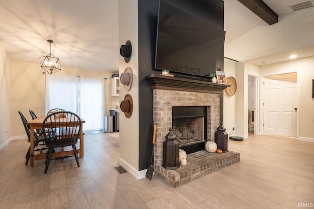 living room with light hardwood / wood-style flooring, an inviting chandelier, beamed ceiling, and a fireplace