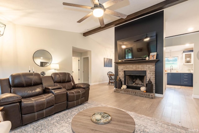 living room with a fireplace, light wood-type flooring, ceiling fan, vaulted ceiling with beams, and sink