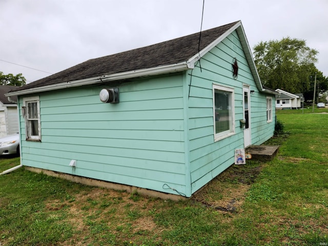 view of side of property featuring a shingled roof and a yard