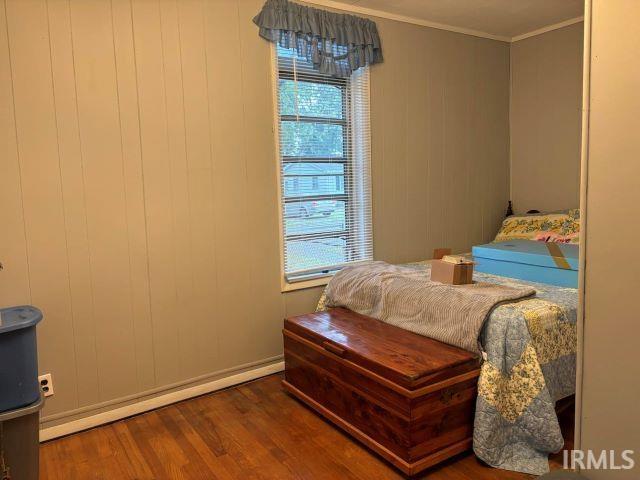 bedroom with multiple windows, ornamental molding, wood walls, and dark hardwood / wood-style floors