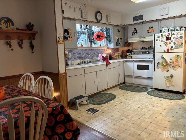 kitchen with sink, ventilation hood, white cabinets, wood walls, and white appliances