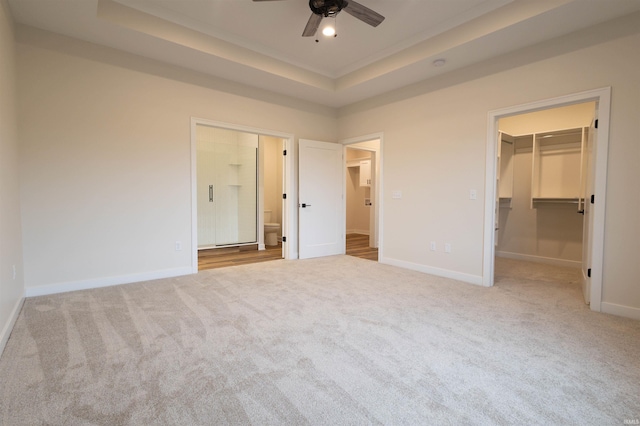 unfurnished bedroom featuring a raised ceiling, a spacious closet, ceiling fan, and light colored carpet