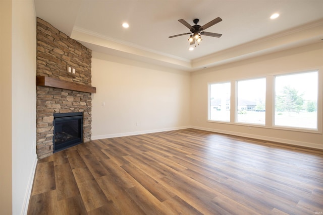 unfurnished living room featuring ceiling fan, crown molding, dark wood-type flooring, and a stone fireplace