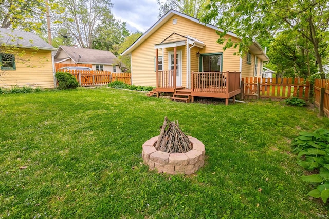 rear view of property with a wooden deck, a fire pit, and a lawn