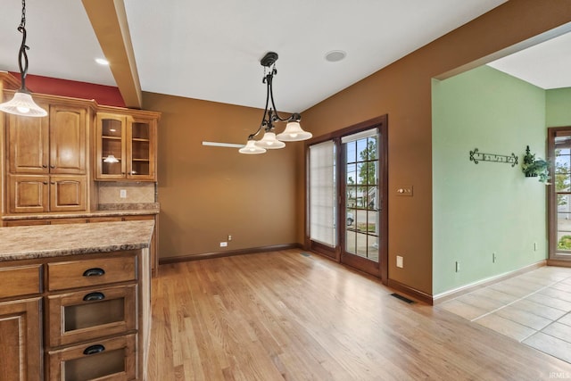 kitchen with light hardwood / wood-style floors, light stone counters, beam ceiling, decorative light fixtures, and a chandelier