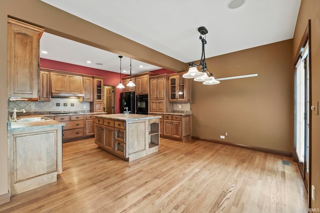 kitchen with pendant lighting, light wood-type flooring, black appliances, a kitchen island with sink, and sink