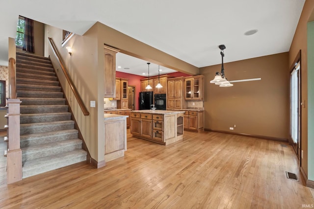 kitchen featuring light wood-type flooring, black appliances, decorative light fixtures, and a kitchen island