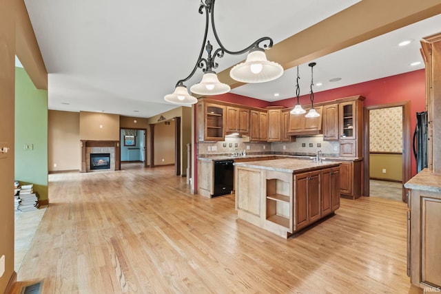 kitchen with hanging light fixtures, a tile fireplace, backsplash, a kitchen island, and light wood-type flooring