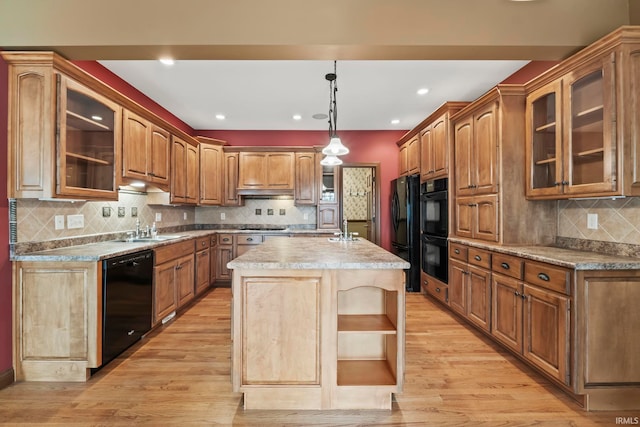 kitchen featuring decorative light fixtures, a center island with sink, backsplash, black appliances, and light hardwood / wood-style floors