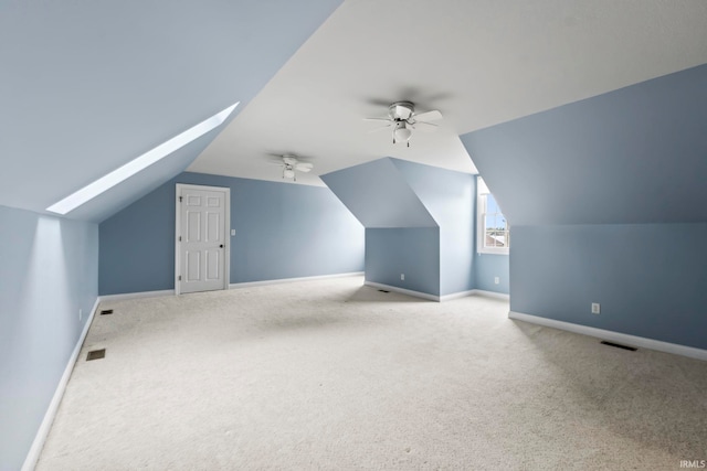 additional living space featuring vaulted ceiling with skylight, ceiling fan, and light colored carpet