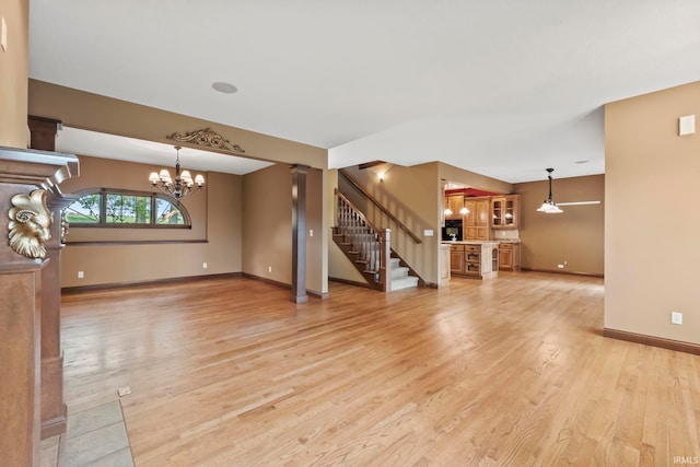 unfurnished living room with ceiling fan with notable chandelier and light hardwood / wood-style flooring