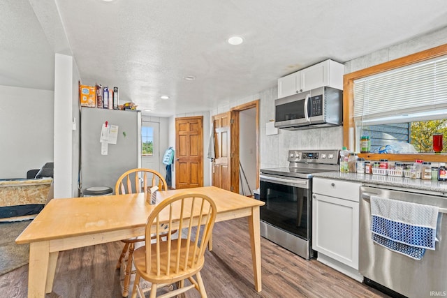 kitchen with a textured ceiling, white cabinets, light hardwood / wood-style flooring, appliances with stainless steel finishes, and light stone countertops