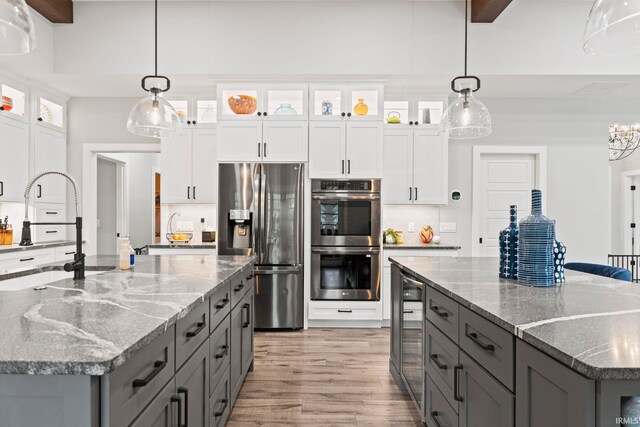 kitchen featuring light hardwood / wood-style floors, a large island with sink, white cabinets, appliances with stainless steel finishes, and decorative light fixtures