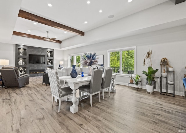 dining room with ceiling fan, beamed ceiling, light hardwood / wood-style flooring, and a high end fireplace