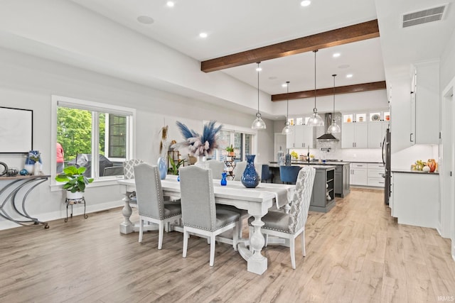 dining space with light hardwood / wood-style floors, sink, and beamed ceiling