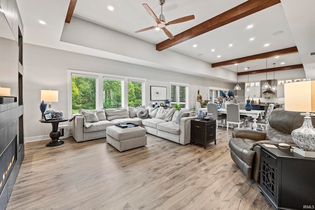 living room featuring light hardwood / wood-style flooring, ceiling fan, beamed ceiling, and a fireplace