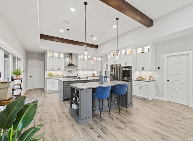 kitchen with pendant lighting, a kitchen island with sink, white cabinets, light hardwood / wood-style flooring, and appliances with stainless steel finishes