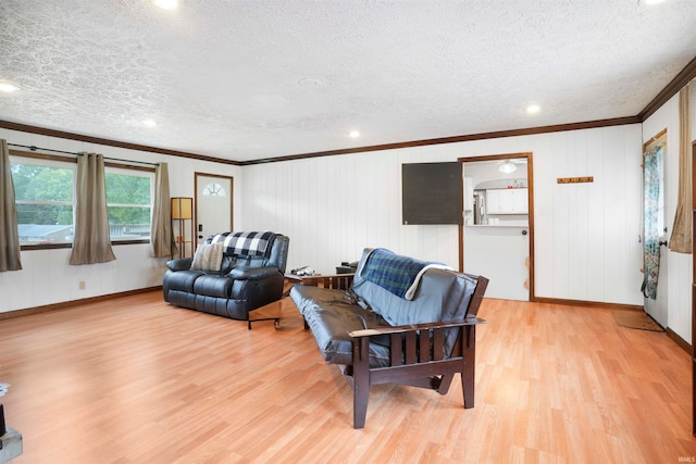 living room featuring a textured ceiling, wooden walls, ornamental molding, and light hardwood / wood-style flooring