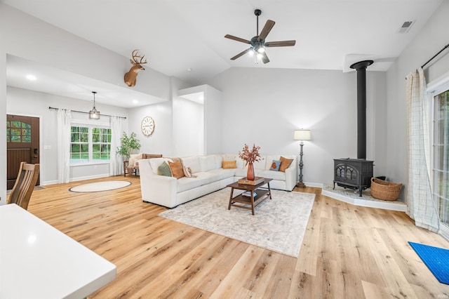 living room with light wood-type flooring, vaulted ceiling, ceiling fan, and a wood stove