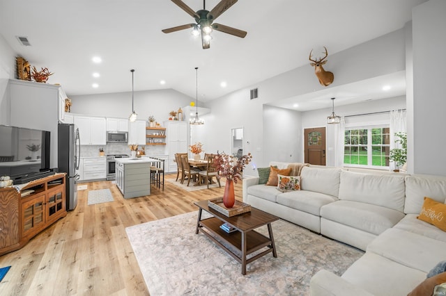 living room with ceiling fan with notable chandelier, light wood-type flooring, and vaulted ceiling