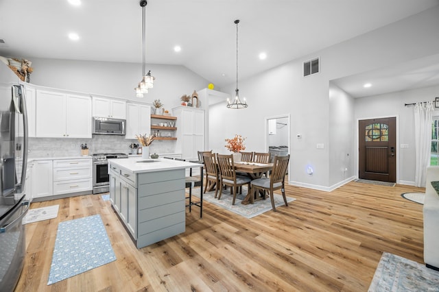 kitchen with white cabinets, hanging light fixtures, appliances with stainless steel finishes, a center island, and light wood-type flooring