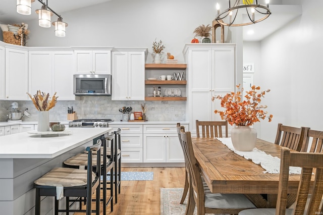 kitchen with hanging light fixtures, light hardwood / wood-style floors, tasteful backsplash, white cabinets, and an inviting chandelier