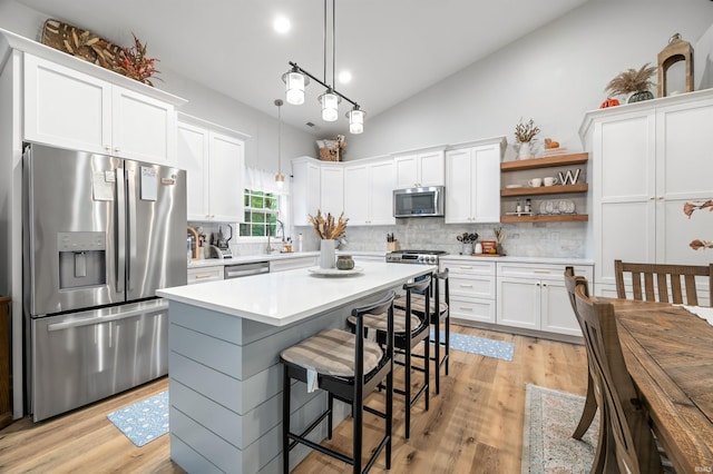 kitchen with appliances with stainless steel finishes, hanging light fixtures, light hardwood / wood-style floors, white cabinetry, and backsplash