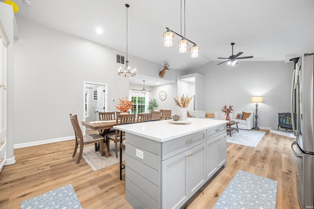 kitchen featuring a center island, ceiling fan with notable chandelier, hanging light fixtures, stainless steel refrigerator, and light hardwood / wood-style flooring