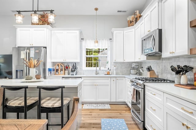 kitchen featuring hanging light fixtures, sink, white cabinetry, stainless steel appliances, and light wood-type flooring