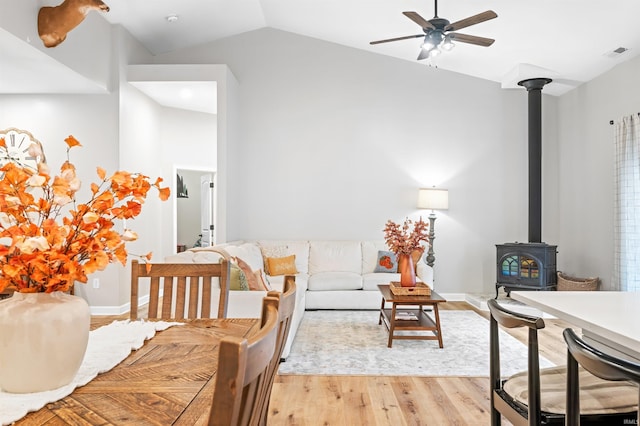 interior space with light hardwood / wood-style floors, vaulted ceiling, ceiling fan, and a wood stove