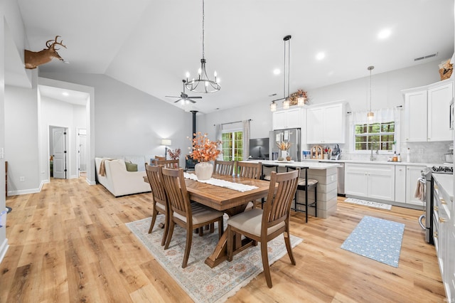 dining space with ceiling fan with notable chandelier, a healthy amount of sunlight, light hardwood / wood-style floors, and vaulted ceiling