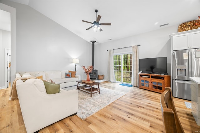 living room with light hardwood / wood-style flooring, a wood stove, vaulted ceiling, and ceiling fan