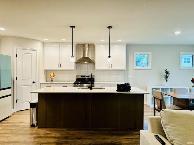 kitchen featuring hanging light fixtures, white cabinets, light wood-type flooring, sink, and wall chimney range hood