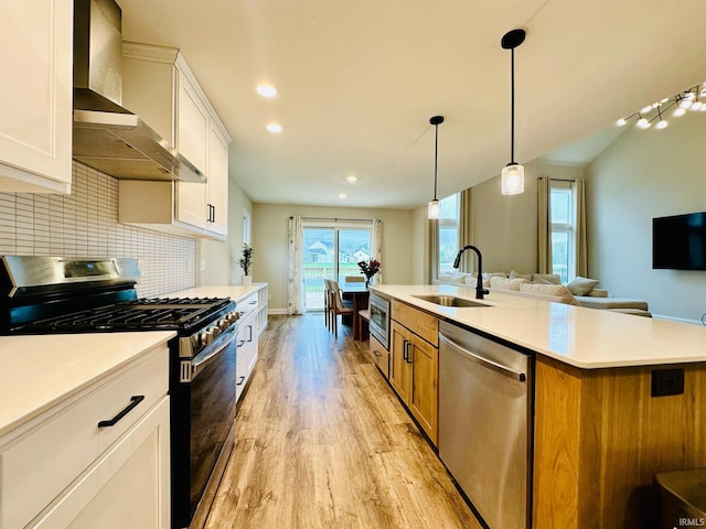 kitchen with sink, a kitchen island, wall chimney range hood, white cabinetry, and appliances with stainless steel finishes