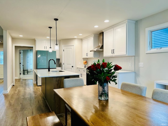 kitchen with hanging light fixtures, a center island with sink, wall chimney range hood, and white cabinets