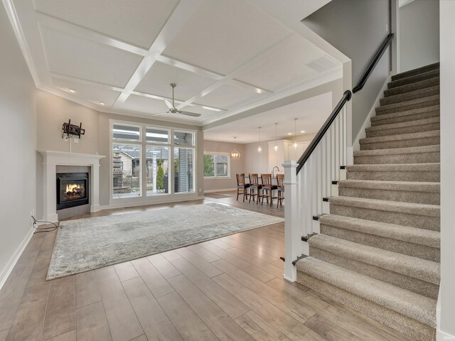 381 Elderwood Ct, Fort Wayne, IN 46845 - interior space featuring ceiling fan with notable chandelier, a glass covered fireplace, stairway, wood finished floors, and coffered ceiling