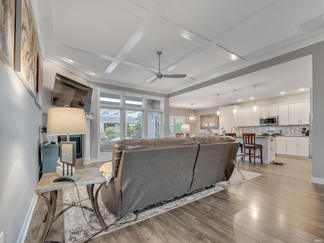 living room with ceiling fan, beamed ceiling, ornamental molding, light hardwood / wood-style flooring, and coffered ceiling