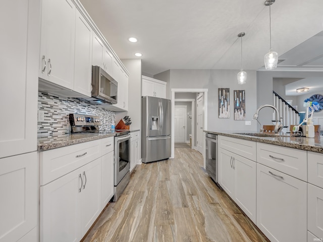 kitchen with light wood-type flooring, light stone counters, sink, white cabinetry, and stainless steel appliances