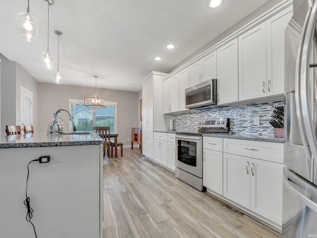 kitchen featuring light wood-type flooring, white cabinets, stainless steel appliances, decorative light fixtures, and stone countertops