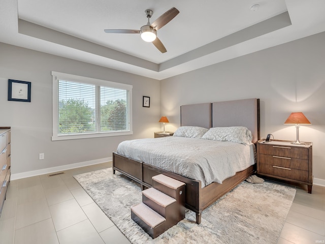 bedroom with ceiling fan, a raised ceiling, and light tile patterned floors