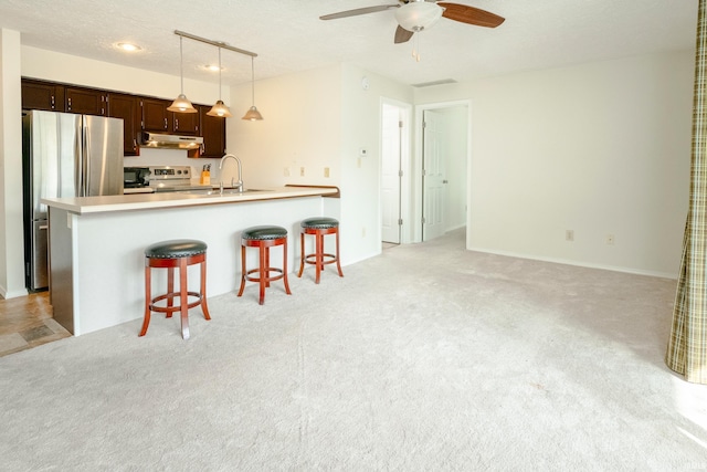 kitchen with dark brown cabinets, a textured ceiling, decorative light fixtures, stainless steel appliances, and a breakfast bar