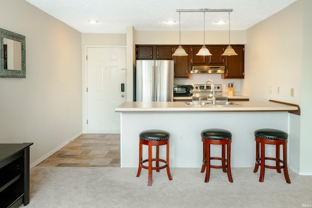 kitchen featuring hanging light fixtures, kitchen peninsula, stainless steel appliances, light carpet, and a kitchen bar