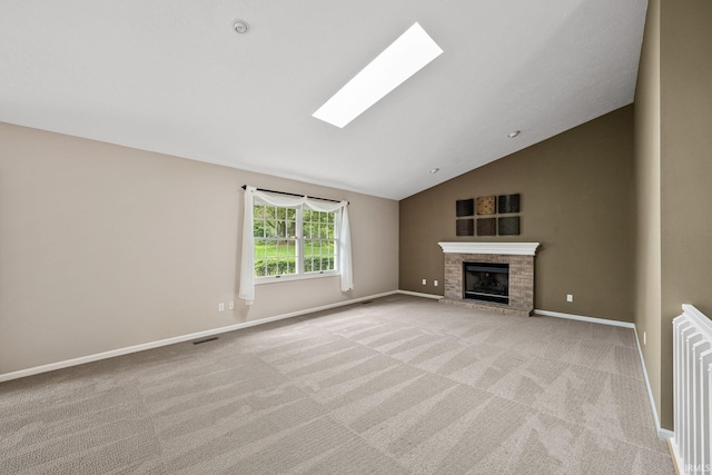 unfurnished living room with vaulted ceiling with skylight, light colored carpet, and a brick fireplace