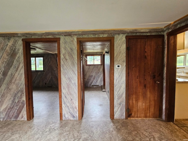 corridor featuring concrete flooring, wooden walls, and a wealth of natural light