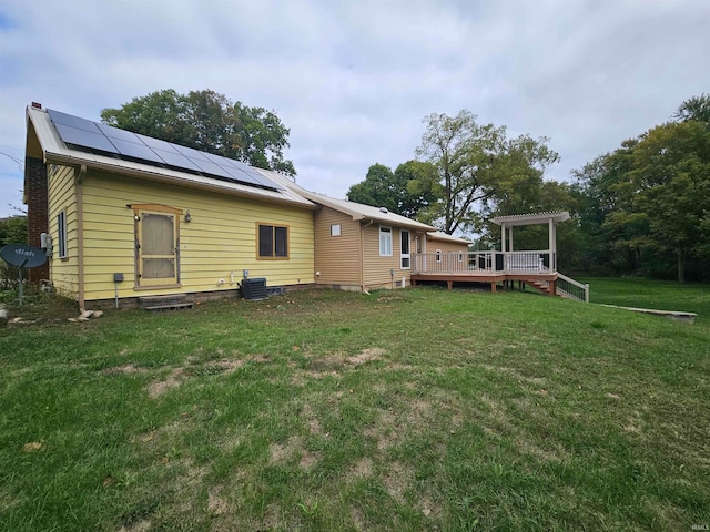 back of property with cooling unit, solar panels, a wooden deck, and a yard