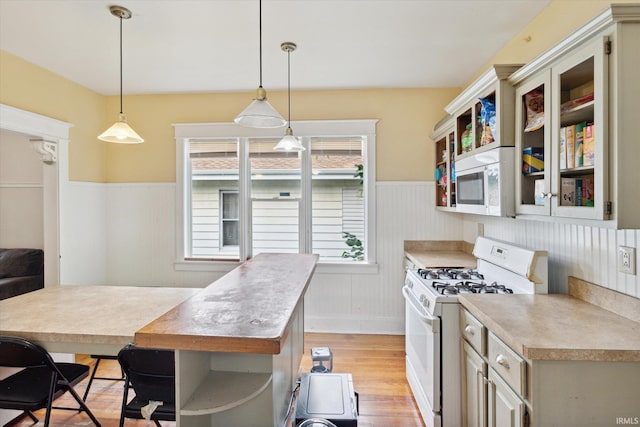 kitchen featuring hanging light fixtures, white appliances, light hardwood / wood-style flooring, and a kitchen bar