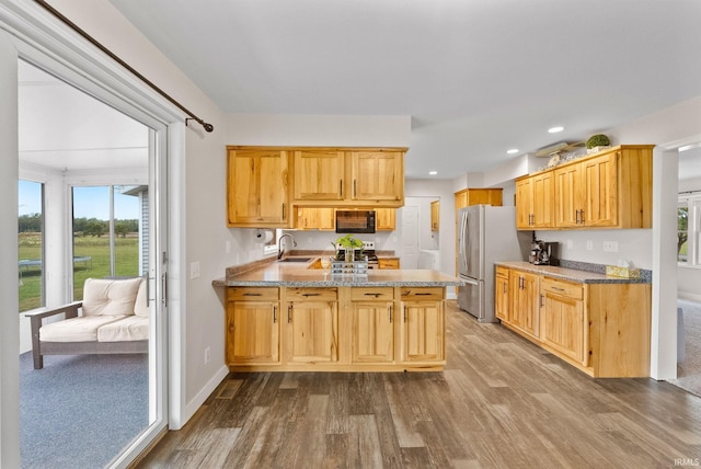 kitchen with appliances with stainless steel finishes, wood-type flooring, kitchen peninsula, and sink