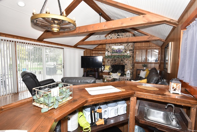 living room with sink, ceiling fan with notable chandelier, wood walls, a fireplace, and vaulted ceiling with beams