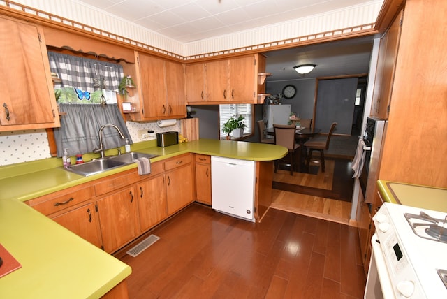 kitchen with kitchen peninsula, sink, white appliances, tasteful backsplash, and dark hardwood / wood-style flooring