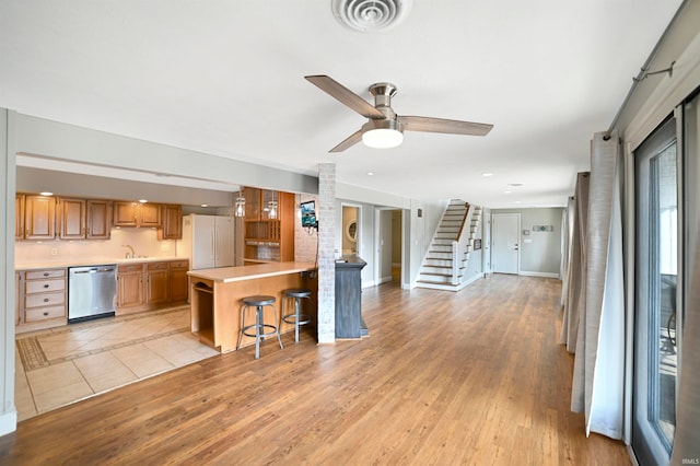 kitchen featuring dishwasher, white refrigerator, kitchen peninsula, light wood-type flooring, and a breakfast bar area